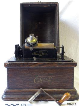 Phonograph with lid off, crank handle on bench in front of machine.