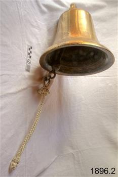 Small brass bell suspended on a wall. Bell has a pull-rope