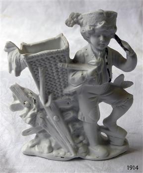White male child figure wearing a hat, standing beside a woven basket