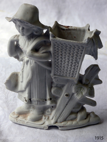 White ornament of girl wearing a hat and carrying a basket on her back
