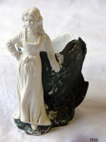 White porcelain ornament of standing female in front of green vase