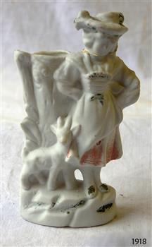 White porcelain figurine of a girl with a goat standing in front of a tree trunk vase