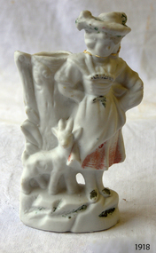 White porcelain figurine of a girl with a goat standing in front of a tree trunk vase