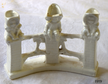White porcelain ornament of three children sitting on fence posts