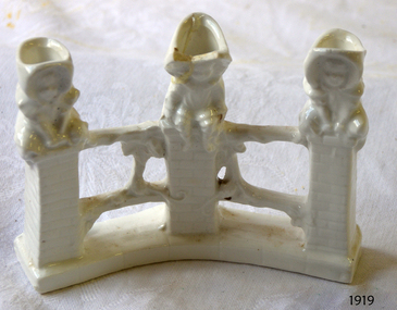 White porcelain ornament of three children sitting on fence posts