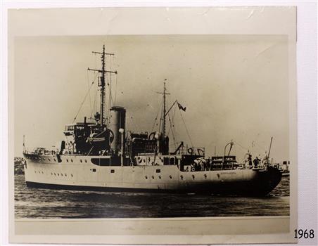 Metal hull, two masts, dark band on top of light funnel, flag flying, figures on deck, name on side