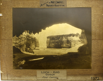 Photograph is mounted and has labels. Image shows cave mouth looking towards sea and rock pillars