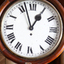 Wood encased white clock face with Roman numerals and maker's name