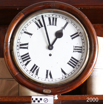Wood encased white clock face with Roman numerals and maker's name