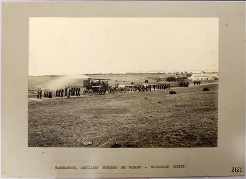 Group of military personnel with several cannon being pulled by a steam driven carriage.