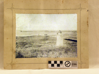 Lighthouse on a hill overlooking bay with ship and jetty