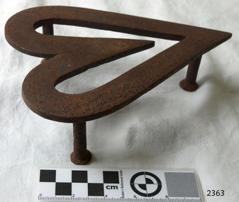 Heart-shaped cast iron trivet standing on three supports. 