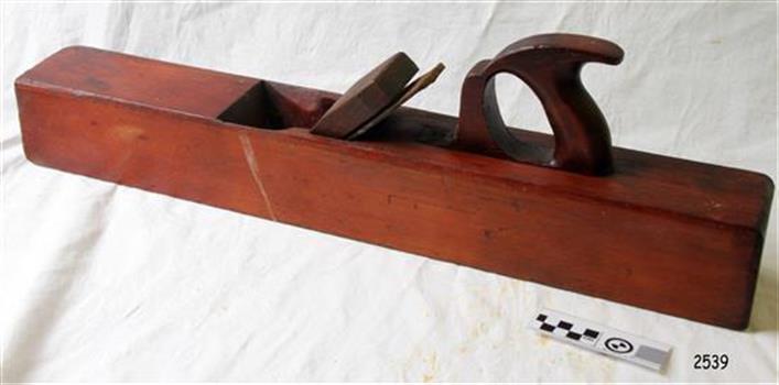 Long wooden plane with blade inserted, wood has red-brown stain.