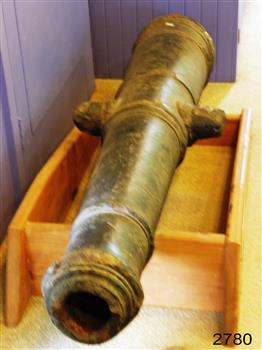 Iron cannon with open end facing viewer. A lug juts out on each side of the cannon.