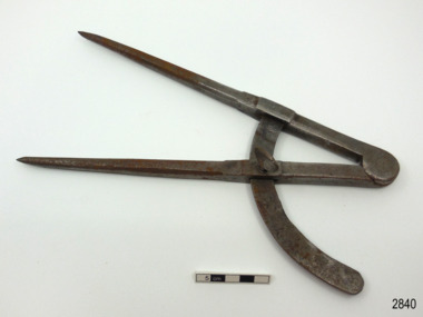 Metal compass has a 90 degree arc and a screw to hold the angle in place. The pointed arms are hinged at the top. There is an inscription on the compass. 