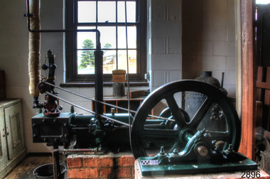 Green panted machine with red painted piston, and wheel attached to a drive blet. 