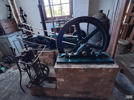Large green painted, spoked fly wheel with a flat belt connected to the governor
