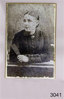 Portrait with woman facing her right, holding a book and leaning on a desk