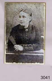 Portrait with woman facing her right, holding a book and leaning on a desk
