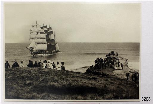 Black and white photograph with seated people observing a fully rigged sailing ship