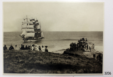 Black and white photograph with seated people observing a fully rigged sailing ship