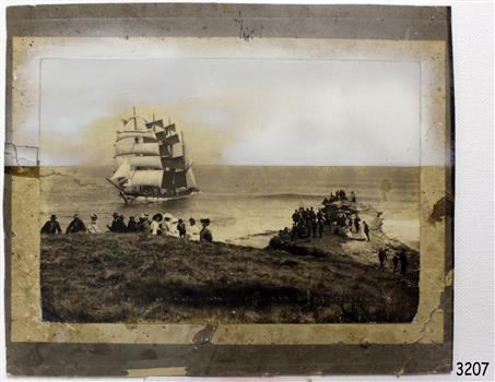Mounted black and white photograph of group of people observing a fully rigged ship 