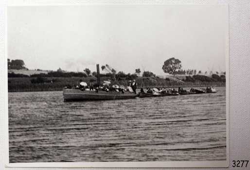 Steam launch on water towing small boats