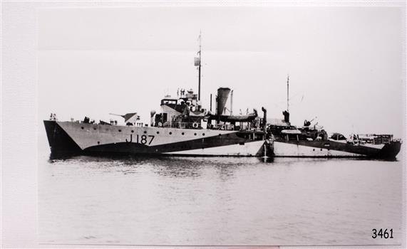 Side profile of steam steam in calm water, standing figures on deck. Ship numbered J187"