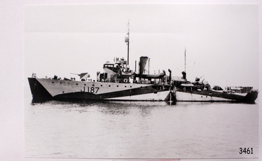 Side profile of steam steam in calm water, standing figures on deck. Ship numbered J187"