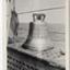 Ship's bell on horizontal surface, inscribed letters around bell, sea and sky as background.