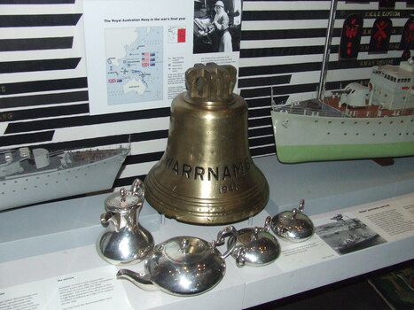Bell on display showing inscription, with WWII RAN items at Australian War Memorial
