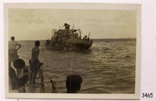 Figures in foreground looking at figures on wrecked ship at sea.