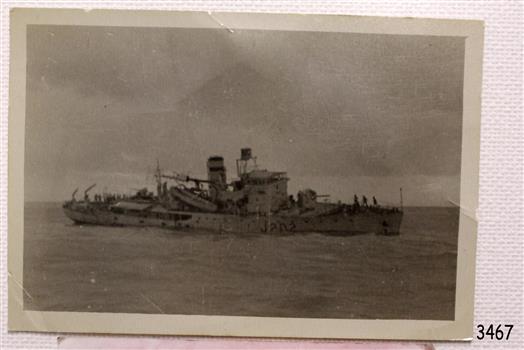 Damaged and sinking ship shown in black and white photograph. Figures are onboard. Ship-type number is clearly visible.