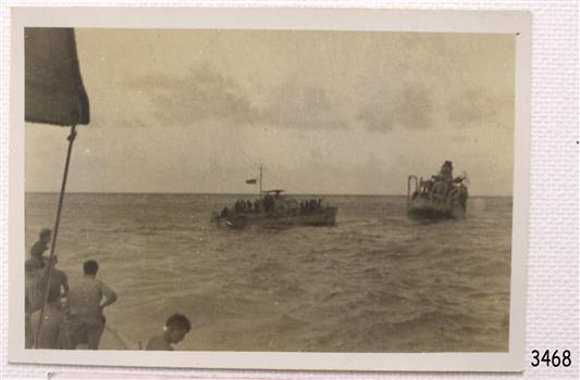 Men look towards small vessel moving towards sinking ship.
