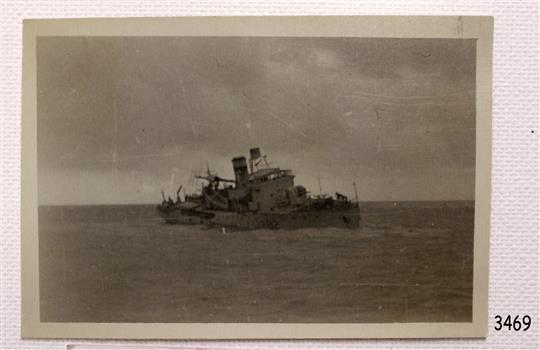 Ship is leaning as it sinks into the sea. Structures on deck are damaged.