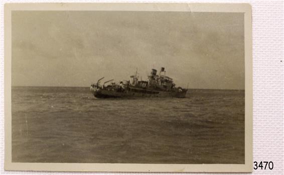 Ship is leaning at a great angle towards the sea on the starboard side. There appears to be figures towards the bow.