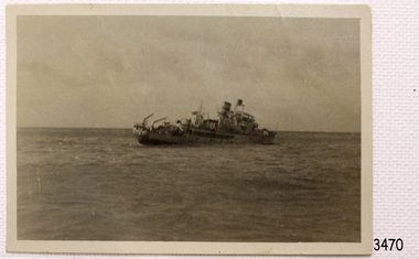 Ship is leaning at a great angle towards the sea on the starboard side. There appears to be figures towards the bow.