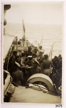 Men onboard the ship are assisting men coming aboard from a small boat
