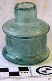 A round hand blown green glass ink bottle with a very uneven break at the top of the neck.
