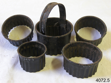 Five round metal pastry cutters, the largest one with a handle. All have corrosion.