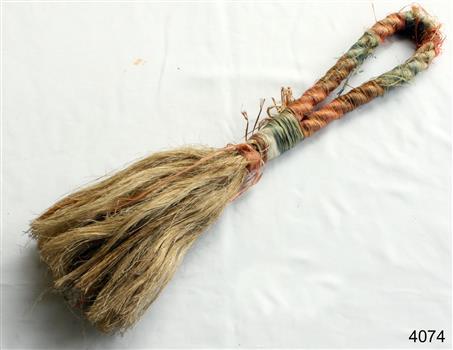 A brush made from a piece of orange and green rope that has been unravelled at the end and tied to form the actual  brush bristles.