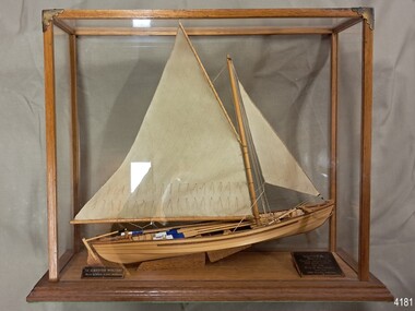 Wooden ship with two sails, mounted in a glass case with wooden frame, Two plaques included.