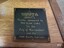 Square black plaque with gold embossed border and sponsor's details
