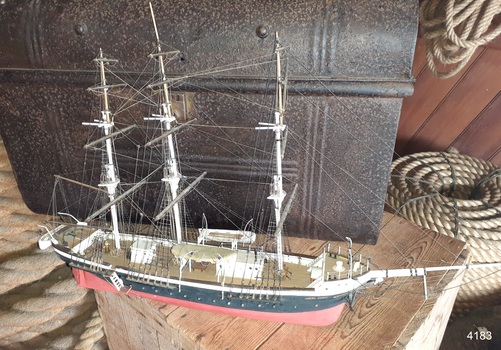 Red and black hulled sailing ship has three lifeboats and rope shrouds as well as a figurehead