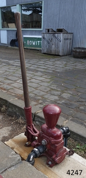 Pump is bolted firmly to timber base. Water pipes are connected to the pump. Timber handle is upright.