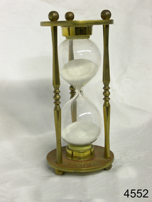 Metal frame with etchings, and a glass hourglass within the frame