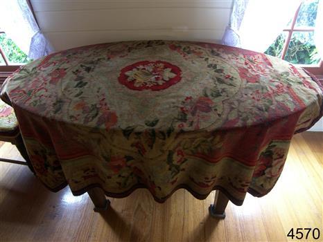Tapestry tablecloth in burgundy and red tones. Border is burgundy, design is floral. 