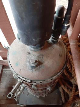 Domed top of boiler has brass fittings and attached chimney base. Tops of wood planks aare held in place by brass bands.
