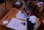 Colour photograph showing re-enactment of a schoolgirl in old fashioned dress writing at her desk. 