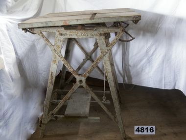 Grey metal machine with square top and treadle foot pedal